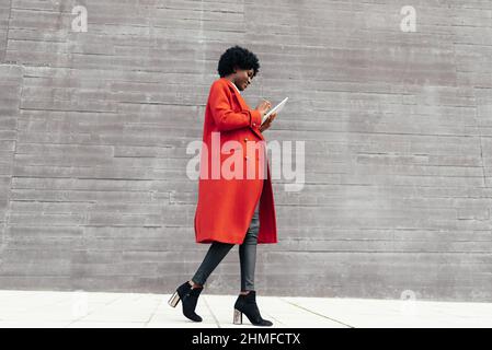 Stylish woman using a digital tablet while walking outdoors on the street. Stock Photo