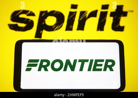 In this photo illustration, Frontier Group Holdings logo is seen on a smartphone screen and Spirit Airlines Inc. logo in the background. Stock Photo