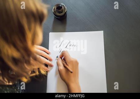 I love you. Calligrapher Young Woman writes phrase on white paper. Inscribing ornamental decorated letters. Calligraphy, graphic design, lettering Stock Photo