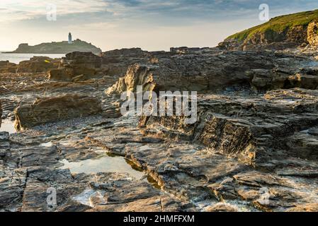 Mid summer warm summer afternoon,near sunset, below the cliffs along the North Cornish coast,dramatic granite and slate rock formations and lighthouse Stock Photo