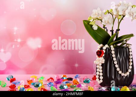 little white orchid in a black pot with pearl necklace, on a pink background with hearts and colorful diamonds Stock Photo