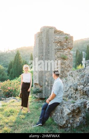 Smiling woman walking towards a man sitting on the ruins of a fortress Stock Photo