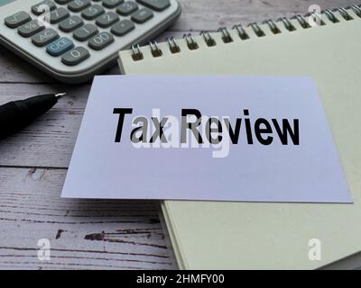 Tax review text on small white card with notepad, pen and calculator background. Tax concept. Stock Photo