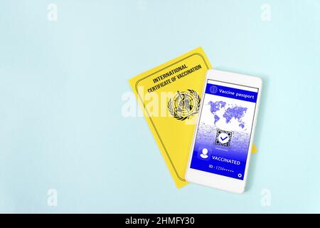 International vaccination record book. Yellow international certificate of vaccination with smartphone displaying valid digital vaccination certificat Stock Photo