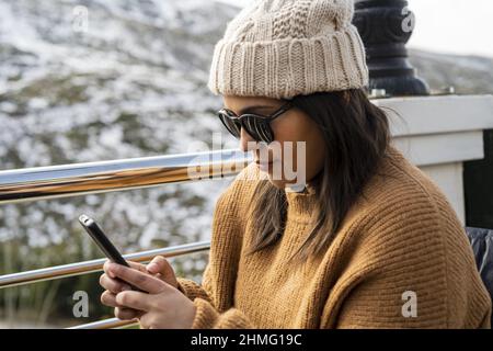 Woman in a hat and wearing sunglasses looking at her smartphone. Stock Photo