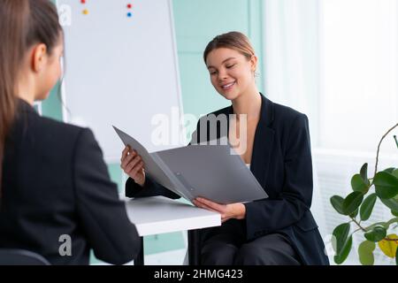 Business meeting. Young blonde woman holding contract while sitting in front of consultant during corporate meeting. Boss discuss ideas with business Stock Photo