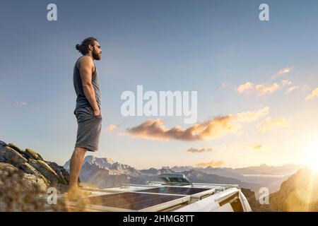Man standing on the roof of his camper van parked in the mountains Stock Photo