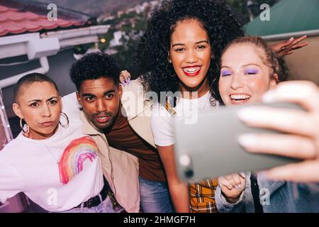 Group of friends posing for a selfie on a rooftop. Four happy friends capturing a picture on a camera phone. Group of multicultural friends having a g Stock Photo