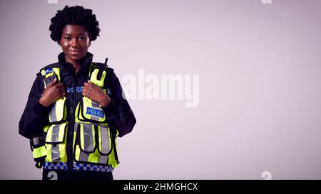 Studio Portrait Of Smiling Young Female Police Officer Against Plain Background Stock Photo