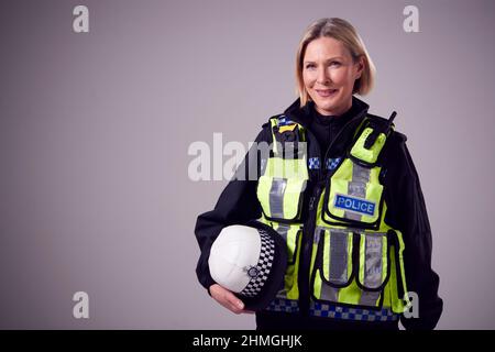Studio Portrait Of Smiling Mature Female Police Officer Holding Hat Against Plain Background Stock Photo
