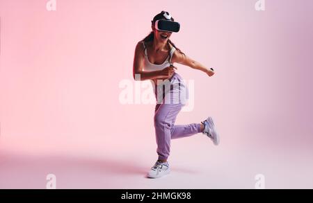 Happy young woman enjoying a virtual reality experience in a studio. Sporty young woman smiling cheerfully while wearing a virtual reality headset. At Stock Photo