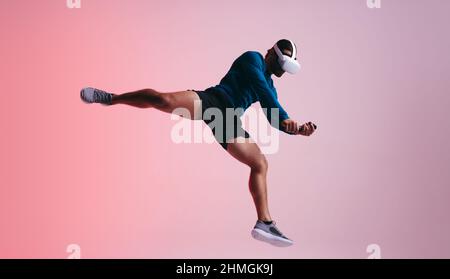 Sportsman jumping mid air while wearing a virtual reality headset. Athletic young man experiencing a 3D simulation. Man enjoying a virtual training se Stock Photo
