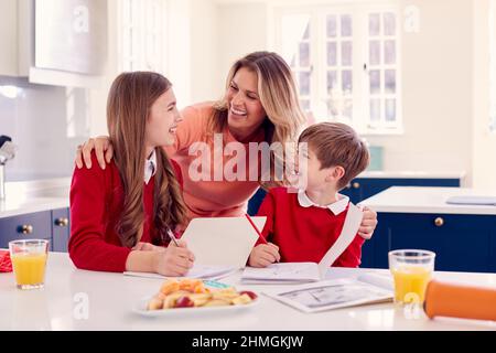 Mother Helping Children In School Uniform Doing Homework At Kitchen Counter Stock Photo