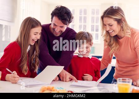 Parents Helping Children In School Uniform Doing Homework At Kitchen Counter Stock Photo