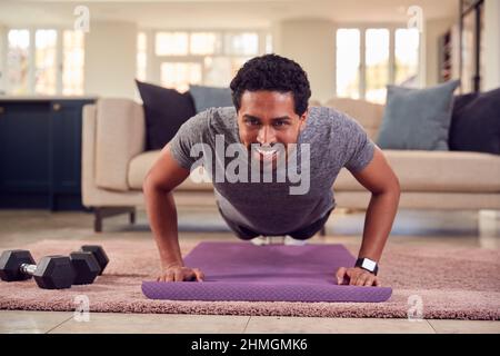 Man In Fitness Clothing At Home In Lounge Doing Press Ups And Exercising With Hand Weights Stock Photo