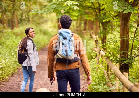 Rear View Of Couple With Pet Dog Hiking Along Path Through Trees In Countryside Stock Photo
