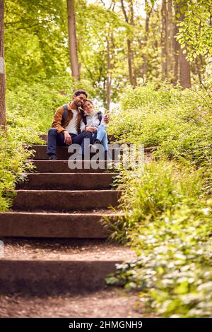 Hiking Couple With Backpacks Sitting On Steps On Path Through Trees In Countryside Together Stock Photo