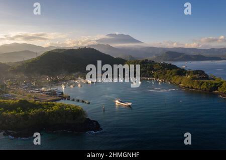Dramatic view of a boat leaving the Padang Bai harbor in eastern Bali with the Agung volcano in the background at sunset in Indonesia Stock Photo