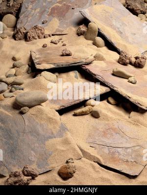 Still life. Close up of slate tiles and pebbles on a sandy beach. Stock Photo