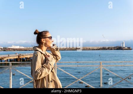 Young adult trendy stylish beautiful caucasian happy smiling woman enjoy walking by Yalta sea embankment on warm sunny day. Female person portrait Stock Photo