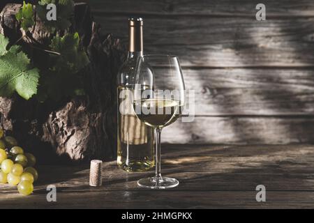 Elegant glass of wine and white wine bottle with grapes and shadows on dark wood background with copyspace. Stock Photo