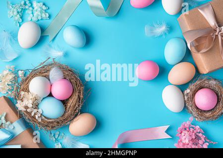 Happy Easter, delicate, pastel background with colored eggs, gift boxes and nests on a blue background. Top view, copy space. Stock Photo