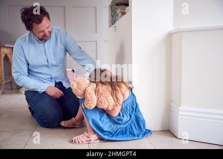 Father Comforting Unhappy Daughter Sitting On Floor Holding Teddy Bear Stock Photo