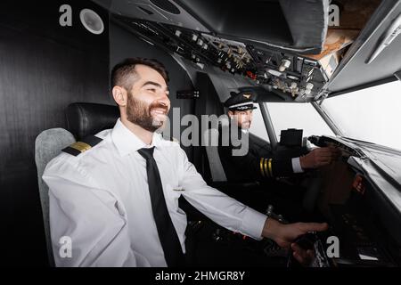 cheerful co-pilot using yoke near captain reaching control panel in airplane simulator Stock Photo
