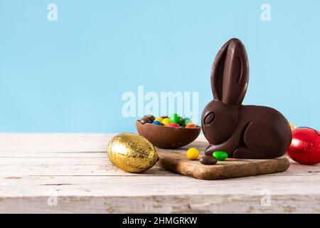Easter chocolate bunny and colorful eggs on wooden table and blue background Stock Photo
