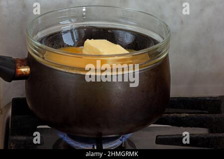 Bain-marie with sugar, butter and honey in glass bowl on saucepan as ingredients of cake medovik on stovetop Stock Photo