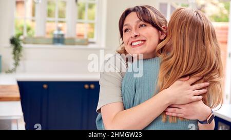Two Female Friends Greeting And Hugging In Kitchen At Home Stock Photo