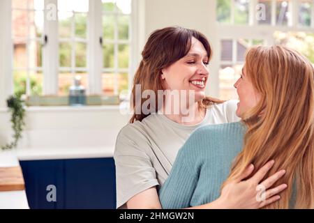 Two Female Friends Greeting And Hugging In Kitchen At Home Stock Photo