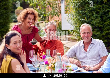 Group Of Mature Friends Talking Around Table At Summer Dinner Party In Garden At Home Stock Photo
