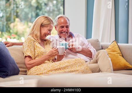 Senior Retired Couple Relaxing On Sofa At Home With Hot Drink Stock Photo