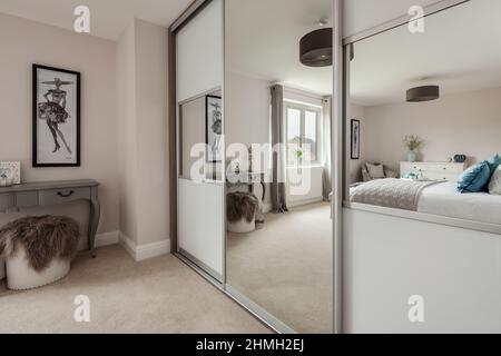 Newport, Essex - March 21 2019: Luxury modern bedroom within vacant new home with bed and furniture reflected in large built in mirrored wardrobe. Stock Photo