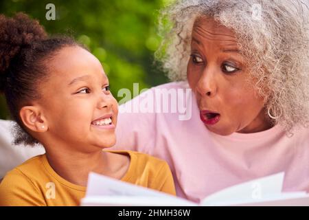 Grandmother Sitting Outdoors With Granddaughter At Home Reading Book Together Stock Photo