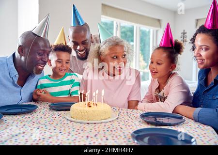 Multi Generation Family Around Table At Home Celebrating Grandmother's Birthday With Cake And Party Stock Photo
