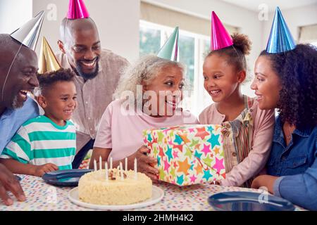Multi Generation Family Around Table At Home Celebrating Grandmother's Birthday With Cake And Party Stock Photo