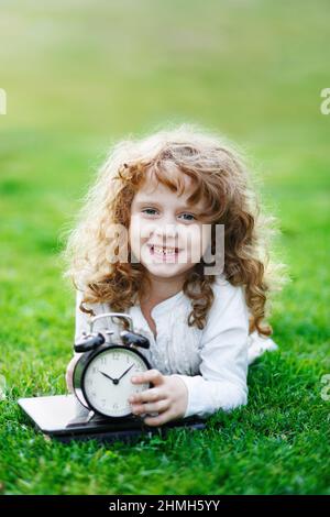 Little schoolgirl resting on lawn in the autumn park. Happy to back to school. Childhood concept. Stock Photo