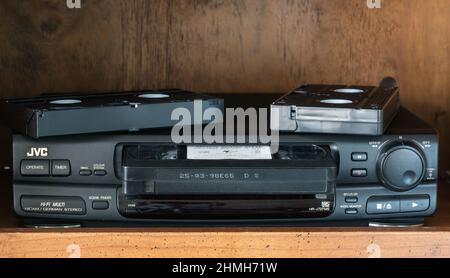 VHS - a classic, high quality  VHS player/recorder in black with gold lettering. On a brown wooden background with VHS cartridge loaded. Extras on top. Stock Photo