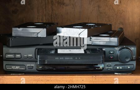 VHS - a classic, high quality  VHS player/recorder in black with gold lettering. On a brown wooden background with VHS cartridge loaded. Extras on top. Stock Photo