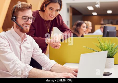 Businessman Wearing Headset Talking To Colleague In Busy Customer Services Centre Stock Photo