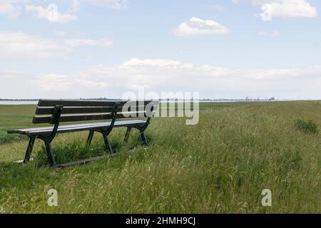 A free bank on the dike near Freiburg invites you to linger. View of the Elbe in Balje, Germany. Stock Photo
