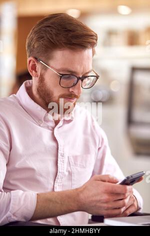 Businessman In Wheelchair With Mobile Phone Sitting At Desk Working On Laptop In Busy Office Stock Photo
