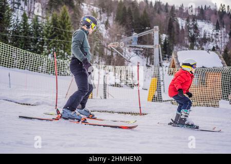 Boy learning to ski, training and listening to his ski instructor on the slope in winter Stock Photo