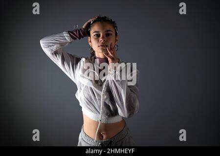 Front view of a young woman with urban style looking at camera while posing with her hands on her face and hair in studio shot. Stock Photo
