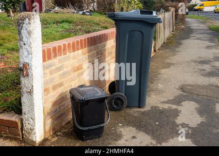 A black wheelie bin and waste food caddy on a pavement outside the front garden wall. Stock Photo