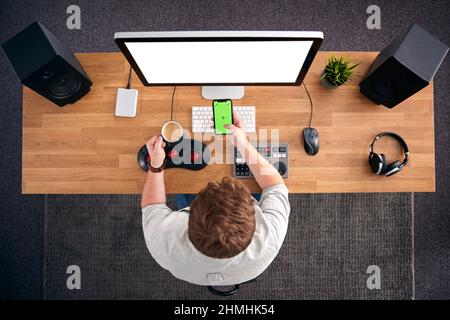 Overhead View Of Male Video Editor Working At Computer In Creative Office Using Mobile Phone Stock Photo