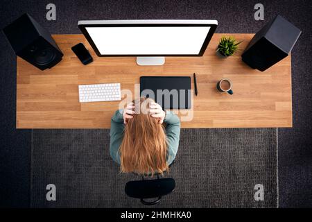 Overhead View Of Stressed Female Graphic Designer At Computer With Head In Hands Stock Photo