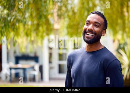 Portrait Of Relaxed Smiling Man Standing In Garden At Home After Retirement Stock Photo